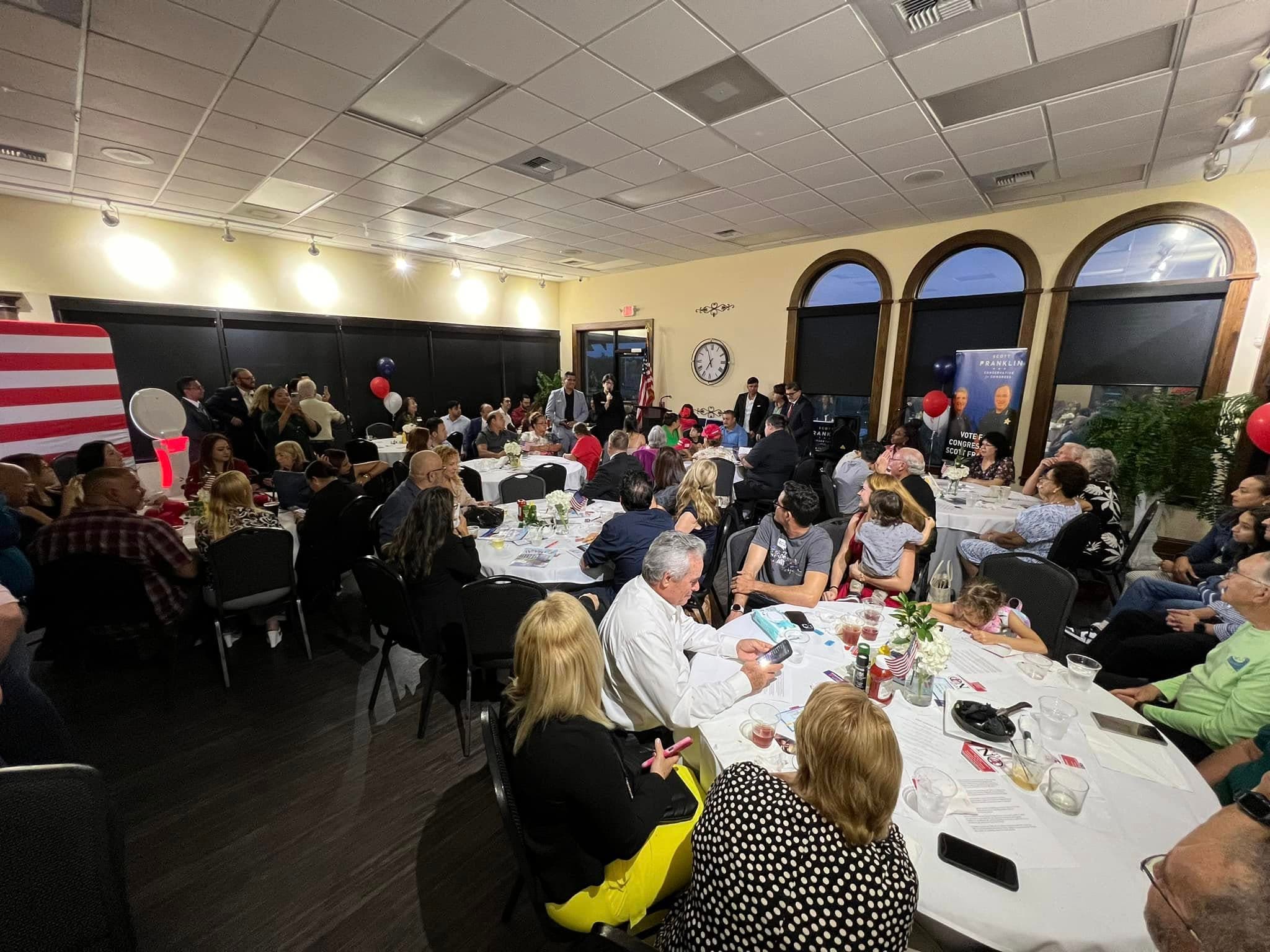 A packed Polk County Republican Executive Committee meeting, with attendees seated at tables and an American flag along the wall